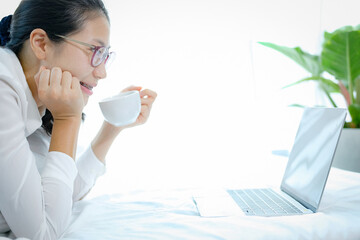 asian woman using computer on bed in bedroom. work remotely at home. leisure lifestyle