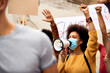 Young black woman wearing protective face mask while shouting through megaphone on anti-racism solidarity protest.