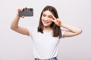 Wall Mural - Portrait of a young attractive woman make peace sign making selfie photo on smartphone isolated on a white background