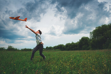 Happy kid playing with toy airplane against stormy summer sky.