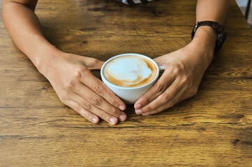 Wall Mural - Female hands holding cups of coffee on rustic wooden table background