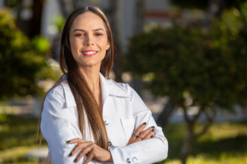 Smiling Brazilian doctor woman in a white coat. Crossed arms.