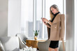 Leinwandbild Motiv Professional businesswoman in luxury office building interior, with skyline in the window, holding smartphone, text and chat