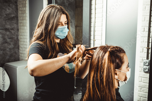 Cuadros en Lienzo Mujer estilista corta el pelo a mujer clienta, con la mascarilla puesta de prote