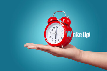 red clock with alarm on hand over blue background, wake up concept in the morning