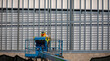 © F Armstrong Photo - Construction worker on blue man lift working on metal prefab building