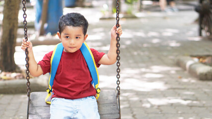 Cute adorable toddler boy swinging on outdoor playground. baby child sitting in chain swing. Active baby on sunny summer day outside.    