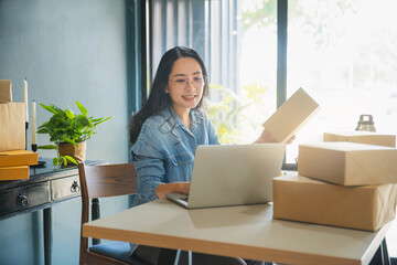 Young business woman working online e-commerce shopping at her shop. Young woman seller prepare parcel box of product for deliver to customer. Online selling, e-commerce.