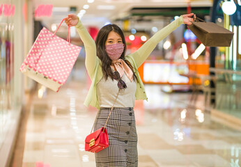 New normal habits - young attractive and happy Asian Chinese woman at shopping mall happy and excited enjoying sale in beauty fashion store carrying shopping bags