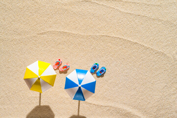 Aerial view of a sandy beach with two  umbrellas, pair of flip flops. Summer and travel concept.