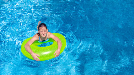 Active young girl in swimming pool aerial top view from above, child relaxes and swims on inflatable ring donut and has fun in water on family vacation, tropical holiday resort
