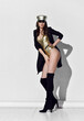 © Dmitry Lobanov - Tall brunette woman in golden swimsuit, cap, black high boots and jacket standing side to us over white wall full body