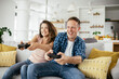 © JustLife - Loving couple playing video games with joysticks in living room. Husband and wife are playing video games at home.