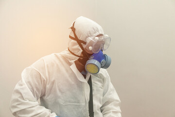 Worker wearing (ppe) protective equipment suit, gloves, mask, and mask cleaning the room with machine of pressurized spray disinfectant water to remove covid-19 coronavirus with sunlight background