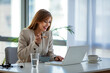 © Dragana Gordic - A businesswoman sits at her desk checking her computer whilst eating a cornflakes from a bowl. She is wearing a smart trouser suit. Working through lunch.
