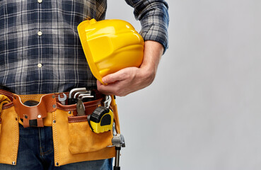 repair, construction and building - male worker or builder with helmet and working tools on belt over grey background