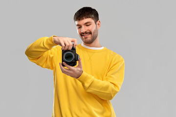 Wall Mural - photography and people concept - smiling young male photographer in yellow sweatshirt taking picture with digital camera over grey background