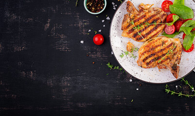 Wall Mural - Grilled pork steaks and salad with tomatoes in plate on dark background. Top view, overhead, copy space