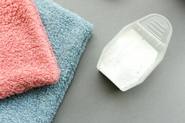 Clean towels and measuring scoop of washing powder on grey background.