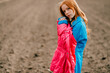 © benevolente - Beautiful strange red head girl in long blue coat and pink warm jacket spends a lot of time on the big empty field.