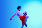 Fototapeta Sport - Passioned for game. Football or soccer player on gradient blue studio background in neon light - motion, action, activity. Concept of sport, competition, winning, action, motion, overcoming. Copyspace