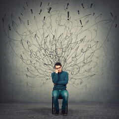 pessimistic, disappointed and depressed businessman keeps hand under cheek, seated on a chair as mes