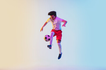 Wall Mural - Kicking in jump, on the run. Football or soccer player on gradient background in neon light - motion, action, activity. Concept of sport, competition, winning, action, motion, overcoming. Copyspace.