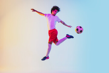 Wall Mural - Kicking in jump, on the run. Football or soccer player on gradient background in neon light - motion, action, activity. Concept of sport, competition, winning, action, motion, overcoming. Copyspace.