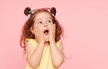 portrait of surprised cute little toddler girl in sunglasses over pink background. child model have 
