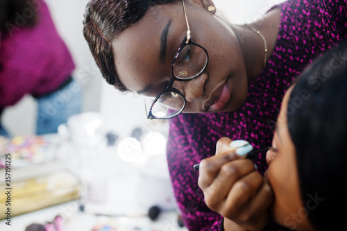 Fotomural African American woman applying make-up by make-up artist at beauty saloon