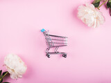 Fototapeta Mapy - Empty toy cart in white peonies frame on pink background. Flat lay. Online shopping