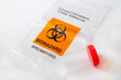Biohazard bag with plastic bottle for sputum specimen collection on white background. Concept of lab test for diagnosis of coronavirus infection. Selective focus
