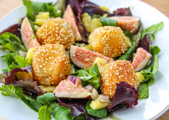 Poster - Fancy salad with goat cheese balls, figs and mango over a wooden table. 