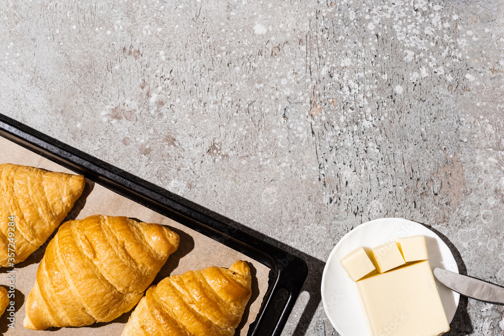 top view of baked delicious croissants on baking tray near butter on concrete grey surface - obrazy, fototapety, plakaty 