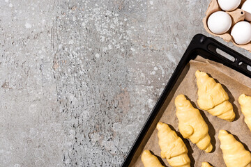 Wall Mural - top view of uncooked croissants on baking tray near eggs on concrete grey surface