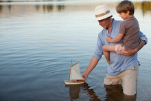 Grandfather And Grandson Wading In Lake With Toy Sailboat