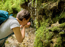 Woman Drinking Water From Her Hands Cupped Under Trickle Of Urach Waterfall In Forest