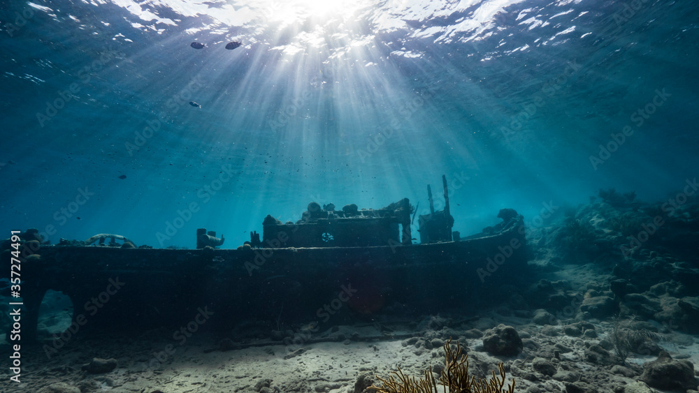 Ship wreck "Tugboat" in  shallow water of coral reef in Caribbean sea / Curacao with view to surface and sunbeam - obrazy, fototapety, plakaty 