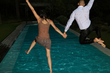 Fully dressed friends jumping into swimming pool