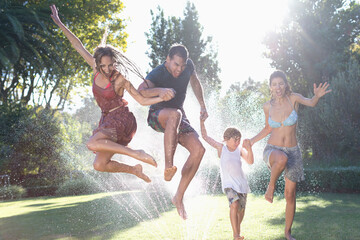 Wall Mural - Family jumping in sprinkler