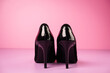 Close up of stylish black high heels shoes on a violet table with a pink background.