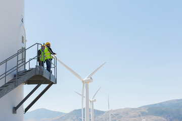 workers standing on wind turbine in rural landscape