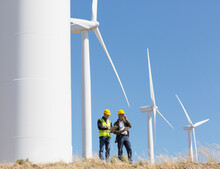Workers Talking By Wind Turbines In Rural Landscape