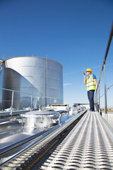 Worker using walkie-talkie on platform above stainless still milk tanker