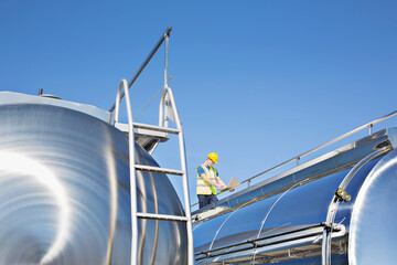 Worker using laptop on platform above stainless steel milk tanker