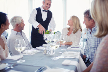 People sitting at restaurant table, waiter pouring white wine