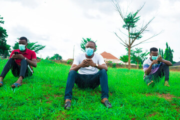 Wall Mural - young black men wearing nose masks, sitting down and using their smartphone