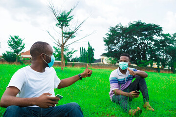 Wall Mural - young black men wearing nose masks, sitting down and using their smartphone