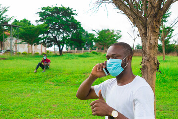 Wall Mural - young black man wearing a nose mask, sitting down and using his smartphone