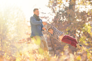 Father spinning son among autumn leaves